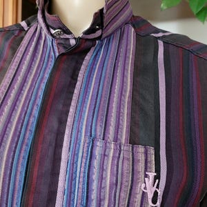 May include: A striped button-down shirt with a purple, blue and black colour scheme. The shirt has a small embroidered logo on the chest.