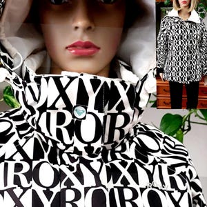 May include: A black and white Roxy jacket with a hood. The jacket features a repeating pattern of the word "ROXY" in large, bold letters. The hood is lined with white fabric. A mannequin is wearing the jacket.