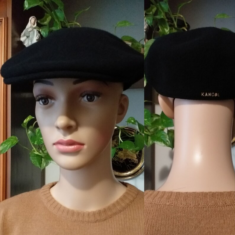 May include: A black wool Kangol brand flat cap with a slightly curved brim. The cap is on a mannequin wearing a brown sweater.