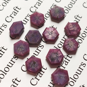 Puede incluir: Colección de gemas hexagonales facetadas en tonos rojo oscuro y púrpura. Las gemas están dispuestas sobre una superficie blanca con las palabras "Colours Craft" impresas en negro.