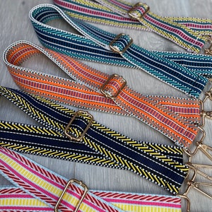 Könnte beinhalten: Fünf bunte gewebte Riemen mit goldenen Metallschließen. Die Riemen haben verschiedene Muster und Farben, darunter Pink, Gelb, Blau, Orange und Schwarz.