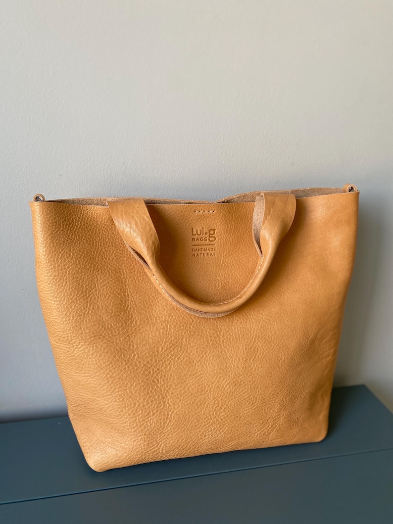 May include: A tan leather tote bag with a top handle and a Luig Bags label that says "Handmade Natural".