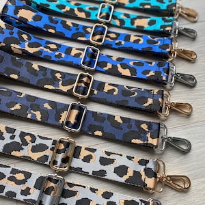 May include: A set of seven colorful leopard print adjustable straps with gold and silver hardware. The straps are made of a woven fabric and have a variety of colors, including blue, teal, and gray.