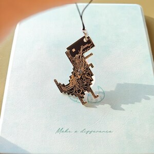 May include: A black and gold pendant in the shape of a pixelated dinosaur, featuring circuit board detailing. The pendant hangs from a black cord. The background is a light blue surface with the words "Make a difference" in cursive.
