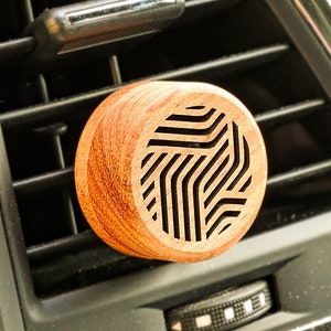 Könnte beinhalten: Ein hölzerner Autolufterfrischer mit geometrischem Muster. Der Lufterfrischer ist braun und hat ein schwarzes geometrisches Design.