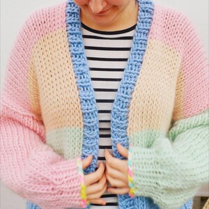 May include: A pastel color block cardigan in pink, yellow, green, and blue. The chunky knit sweater has a blue border and sleeves. The person is wearing a black and white striped shirt underneath.