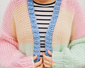 May include: A pastel color block cardigan in pink, yellow, green, and blue. The chunky knit sweater has a blue border and sleeves. The person is wearing a black and white striped shirt underneath.
