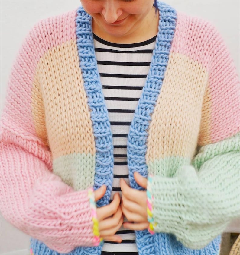 May include: A pastel color block cardigan in pink, yellow, green, and blue. The chunky knit sweater has a blue border and sleeves. The person is wearing a black and white striped shirt underneath.