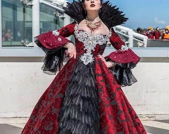 May include: A floor-length gown featuring a red and black floral brocade pattern, a high black feather collar, and a central panel of black feathers. The dress has long flared sleeves with black ruffled cuffs and white lace detailing at the bodice.