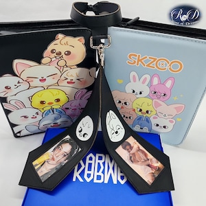 Può includere: Choker in pelle nera con chiusura argentata e due ciondoli neri con foto e facce di cartoni animati. I ciondoli sono collegati a una scatola blu. Due pochette con cerniera con disegni di personaggi dei cartoni animati sullo sfondo.