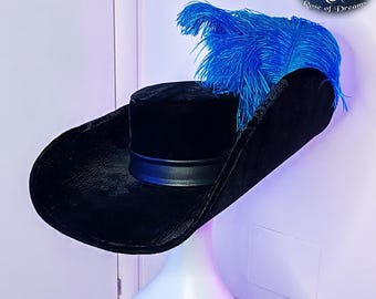 May include: A black velvet hat with a wide, curved brim and a cylindrical crown featuring a smooth black band. A large, vibrant blue ostrich feather plume is attached to the side of the hat. The logo R&D Rose of Dreams is visible in the corner.