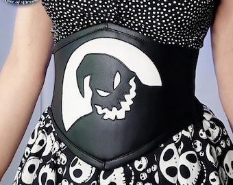 May include: A black waist corset featuring a large white applique of a jagged-toothed character silhouette. The corset is worn over a black and white polka dot top and a skirt patterned with white skull-like faces on a black background.