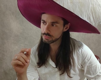 May include: A wide-brimmed deep magenta velvet hat featuring a large, voluminous white ostrich feather plume attached to the side. The hat has a structured, rounded crown and a broad, slightly upturned brim, creating a bold and dramatic silhouette.