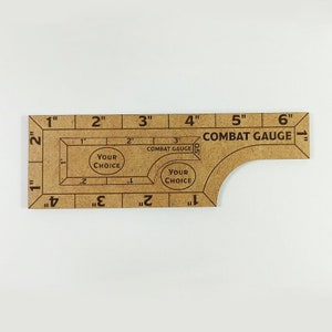 May include: A brown wooden ruler with a curved edge and a scale marked in inches. The ruler has the text "COMBAT GAUGE" printed on it. The ruler also has two circles with the text "YOUR CHOICE" printed inside them.