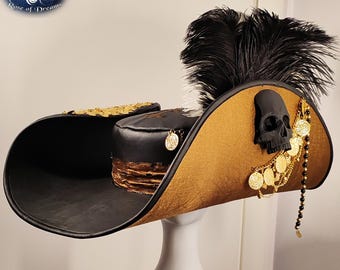 May include: A pirate hat with a black skull, gold coins, and a black feather. The hat has a gold and black color scheme with a decorative gold trim. The hat is displayed on a white mannequin head.