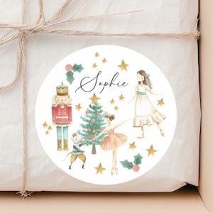 May include: A round sticker featuring a watercolor illustration of a Nutcracker, a Christmas tree, a ballerina, and a girl in a white dress. The sticker has gold stars and holly accents, with the name "Sophie" in script.