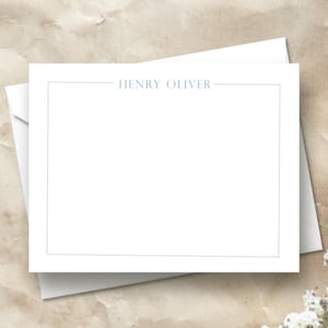 May include: White stationery with a light blue border and the name "HENRY OLIVER" printed at the top. The stationery is on top of a white envelope. The background is a textured, light brown surface with white flowers.