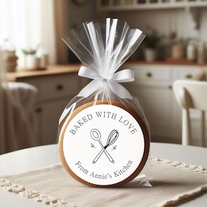 Puede incluir: Una pegatina redonda blanca con texto negro que dice "Baked with Love from Annie's Kitchen". La pegatina presenta una ilustraci&oacute;n en blanco y negro de una cuchara de madera y un batidor cruzados.