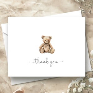 Op de afbeelding: Een witte bedankkaart met een illustratie van een bruine teddybeer en de tekst "dankjewel" in cursief.