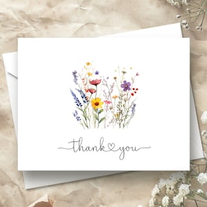 May include: A white card with a watercolor illustration of a bouquet of wildflowers in shades of purple, yellow, pink, and red. The text "thank you" is written in black cursive with a heart symbol between the words.