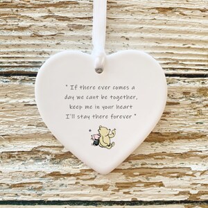 May include: White heart-shaped ornament with a white ribbon for hanging. The ornament features a quote: "If there ever comes a day we can't be together, keep me in your heart, I'll stay there forever." A small illustration of Winnie the Pooh and Piglet is at the bottom.
