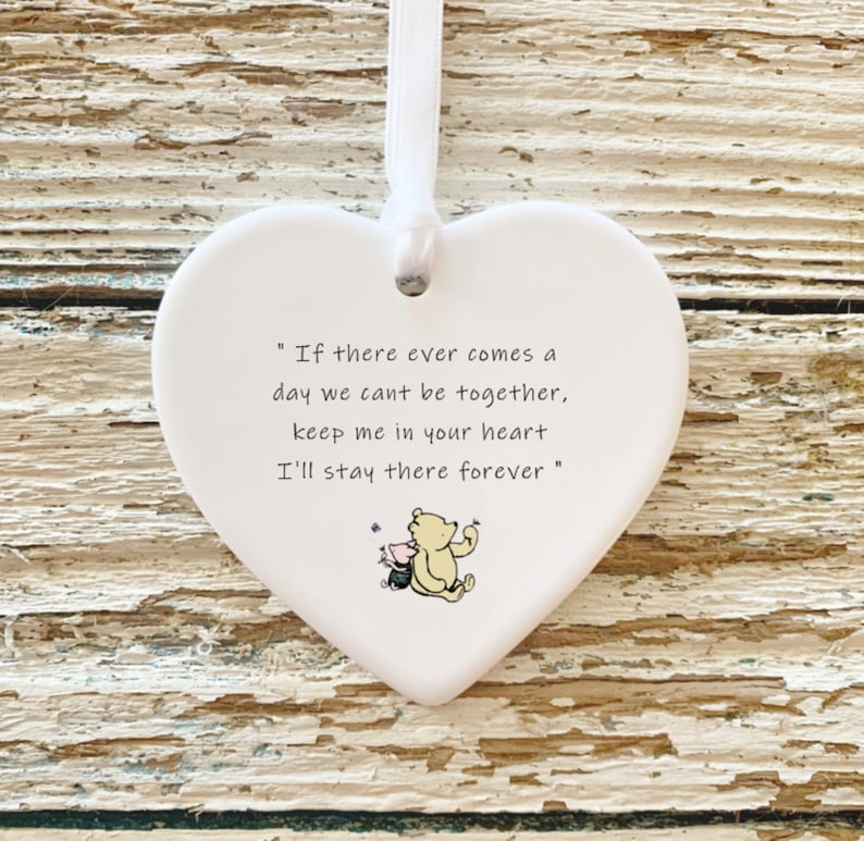 May include: White heart-shaped ornament with a white ribbon for hanging. The ornament features a quote: "If there ever comes a day we can't be together, keep me in your heart, I'll stay there forever." A small illustration of Winnie the Pooh and Piglet is at the bottom.