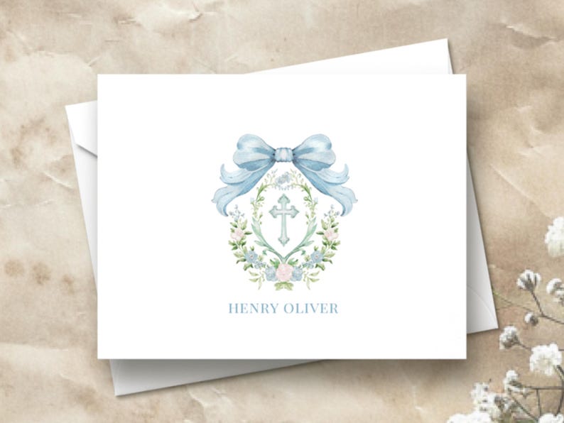 May include: A white card with a blue watercolor bow and floral wreath surrounding a silver cross. The text "HENRY OLIVER" is printed below the wreath.