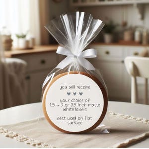 May include: A round cookie in a clear cellophane bag tied with a white ribbon. The cookie has a white label with text that reads "you will receive" and "your choice of 1.5 ~ 2 or 2.5 inch matte white labels".