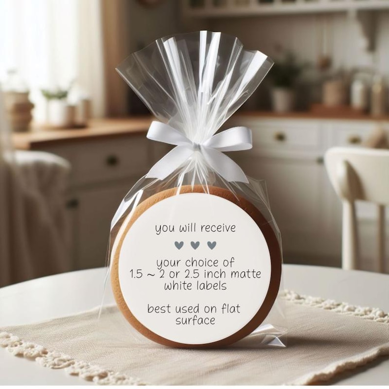 May include: A round cookie in a clear cellophane bag tied with a white ribbon. The cookie has a white label with text that reads "you will receive" and "your choice of 1.5 ~ 2 or 2.5 inch matte white labels".