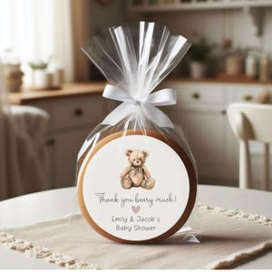 May include: A round, wooden cookie with a white sticker featuring a brown teddy bear and the text "Thank you beary much! Emily & Jacob's Baby Shower".