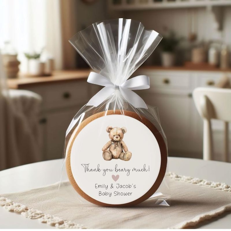 May include: A round, wooden cookie with a white sticker featuring a brown teddy bear and the text "Thank you beary much! Emily & Jacob's Baby Shower".