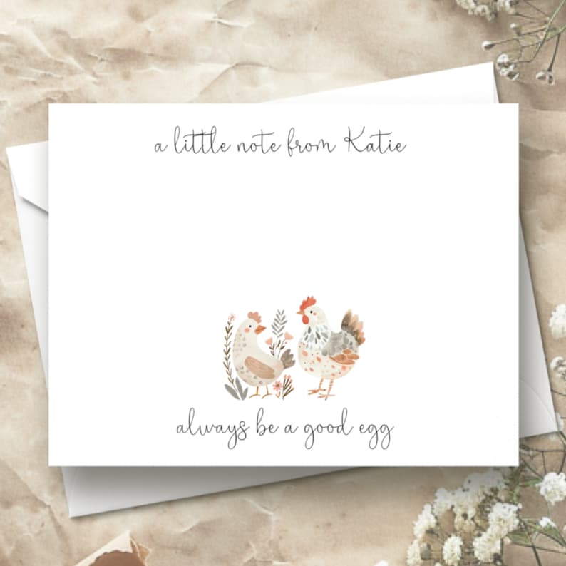Puede incluir: Una tarjeta blanca con un mensaje escrito a mano que dice "a little note from Katie" y "always be a good egg". La tarjeta presenta una ilustraci&oacute;n de acuarela de dos pollos con flores.