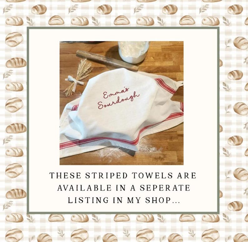 May include: A white kitchen towel with red stripes and the embroidered text Emma's Sourdough, draped over a wooden surface. A wooden rolling pin and a small bundle of wheat stalks are placed nearby, along with a small bowl containing white flour.