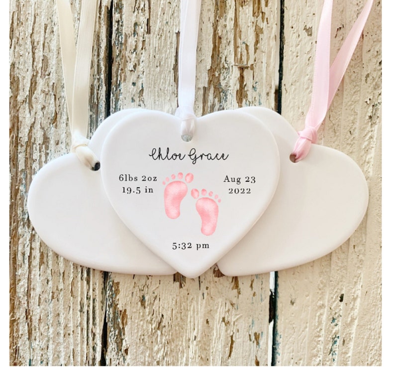 May include: Two white ceramic heart-shaped ornaments with pink footprints and the text "Chloe Grace", "6 lbs 2 oz", "19.5 in", "Aug 23 2022", and "5:32 pm".