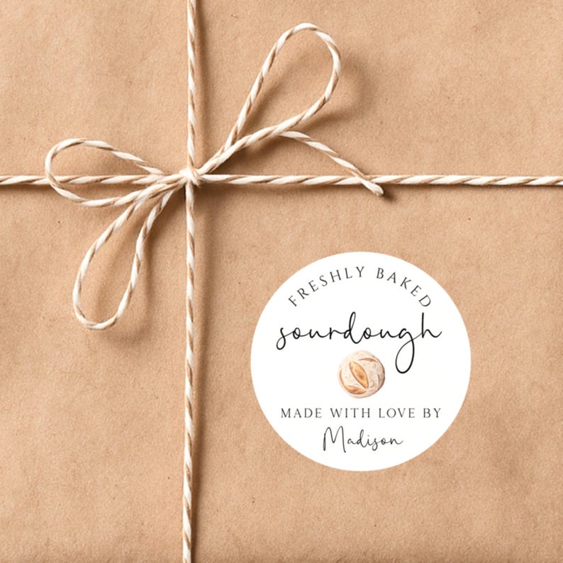 May include: A brown paper package tied with twine, featuring a white circular label. The label reads "FRESHLY BAKED sourdough" with a watercolor illustration of bread and "MADE WITH LOVE BY Madison."