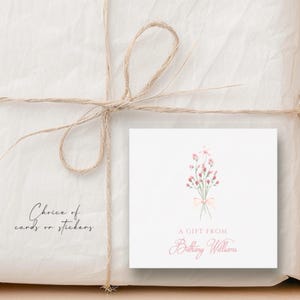 May include: A white gift tag with a pink watercolor bouquet of flowers tied with a pink ribbon. The text "A Gift From Bethany Williams" is printed in pink below the flowers.