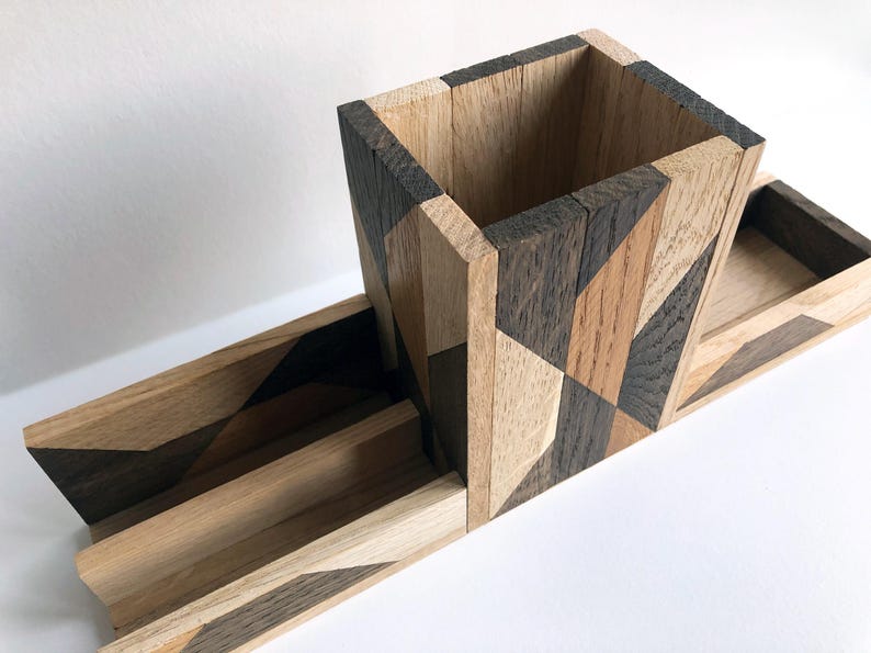 May include: A wooden desk organizer with a geometric pattern in shades of brown and black. The organizer has a tall, square pencil holder and a long, rectangular tray.