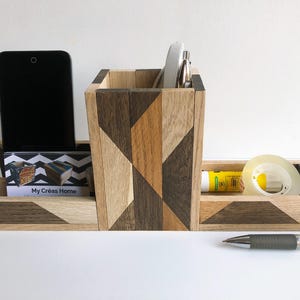 May include: A wooden desk organizer with a geometric pattern in shades of brown and beige. It has compartments for a phone, business cards, pens, and other office supplies. The organizer is labeled "My Creas Home".