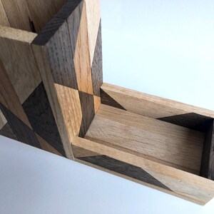 May include: A wooden box with a geometric pattern made of different shades of wood. The box has a long, narrow opening on the side.
