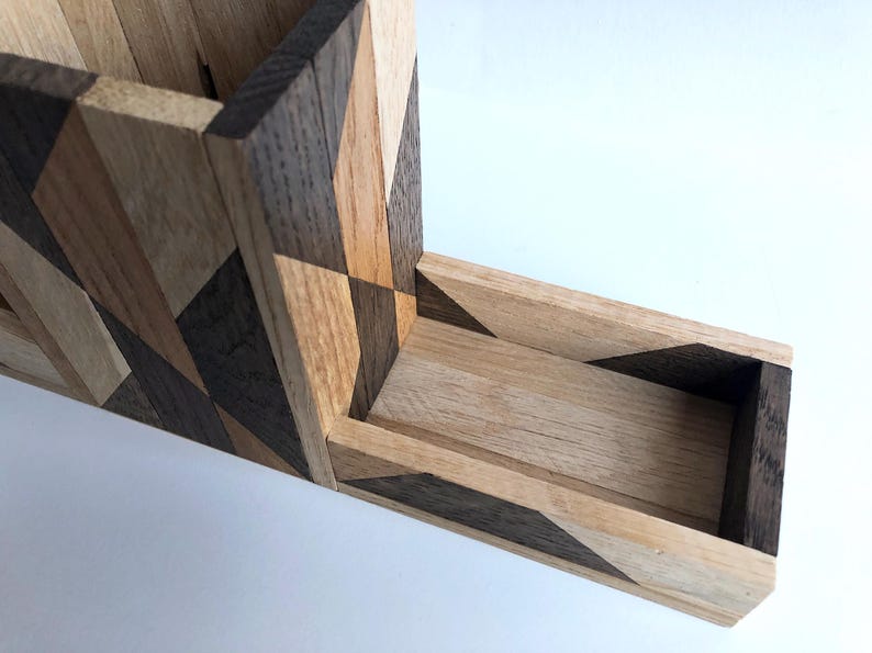 May include: A wooden box with a geometric pattern made of different shades of wood. The box has a long, narrow opening on the side.