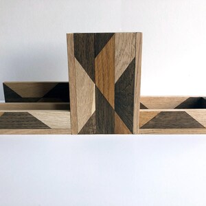 May include: A wooden desk organizer with a geometric pattern in shades of brown, black, and beige. The organizer has three compartments, one tall and two shorter.