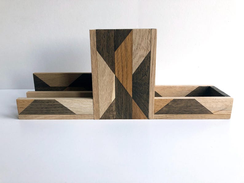 May include: A wooden desk organizer with a geometric pattern in shades of brown, black, and beige. The organizer has three compartments, one tall and two shorter.