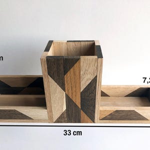 May include: A wooden desk organizer with geometric patterns in shades of brown, black, and beige. The organizer has a central compartment measuring 12 inches tall and two smaller compartments measuring 7.2 inches wide. The overall length of the organizer is 33 inches.