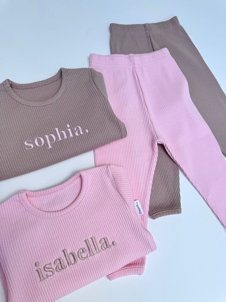 May include: Two sets of ribbed pajamas, one pink and one brown, with the names "sophia" and "isabella" embroidered on the shirts.
