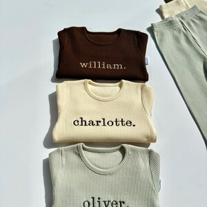 May include: Three long-sleeved shirts in brown, cream, and green with the names "william", "charlotte", and "oliver" embroidered on them.