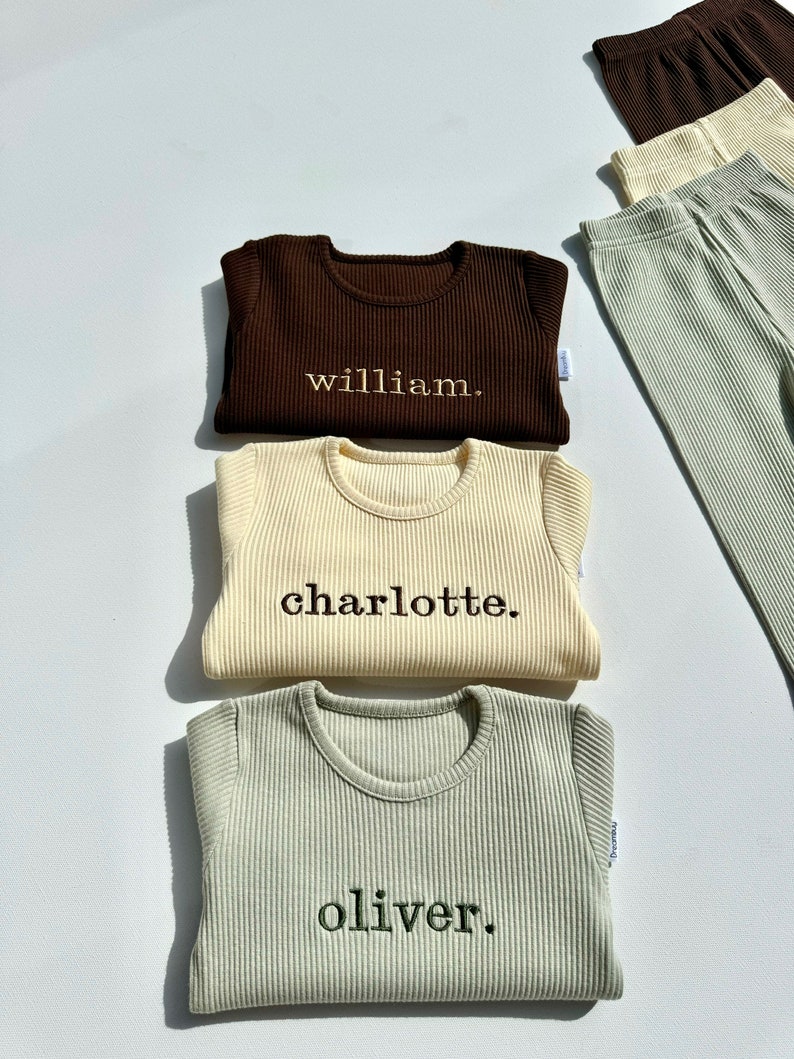 May include: Three long-sleeved shirts in brown, cream, and green with the names "william", "charlotte", and "oliver" embroidered on them.