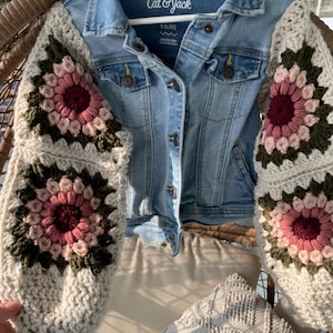 May include: A light blue denim jacket with crocheted sleeves. The sleeves feature a floral design in shades of pink, burgundy, and green on a cream background. The jacket is labeled "Cat & Jack" and is size 5 (6/6x).