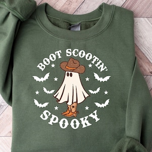 May include: Green sweatshirt with a white ghost wearing a cowboy hat and boots. The text "BOOT SCOOTIN' SPOOKY" is printed on the front.