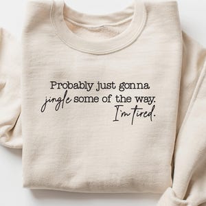 Puede incluir: Sudadera color crema con el texto "Probably just gonna jingle some of the way. I'm tired." en escritura negra. Las mangas est&aacute;n enrolladas. Una prenda casual y c&oacute;moda, ideal para el uso diario.