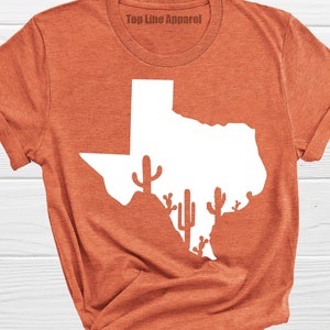 May include: A rust-colored t-shirt with a white outline of the state of Texas and cactus silhouettes. The text "Top Line Apparel" is printed on the shirt.